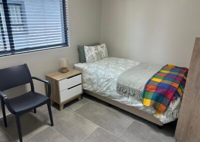 A resident bedroom with a single bed, bedside table and armchair