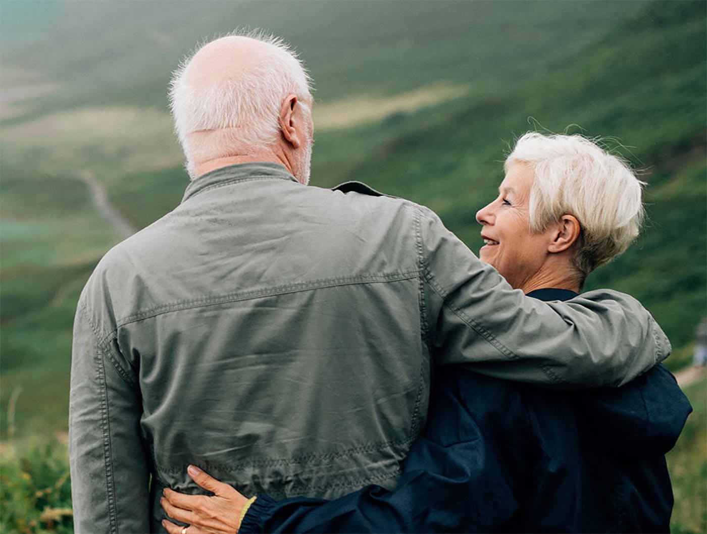 An elderly couple standing outdoors with their arms around each other